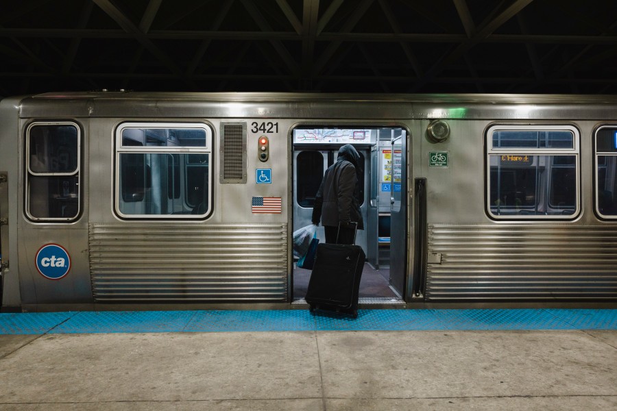 A person carrying his belongings and a bag of Night Ministry supplies boards a Blue Line train late at night.