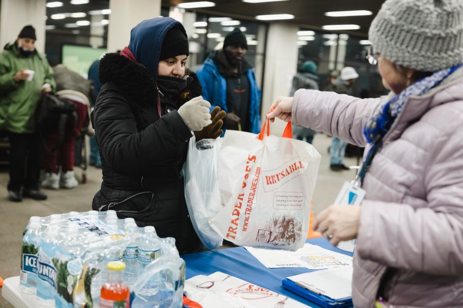 Michela Leone receives a plastic bag containing a meal, water and various health items from outreach worker Doris Rosanova at the Forest Park Blue Line station in March.